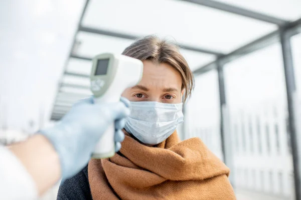 Temperatura de medição de uma jovem mulher na máscara facial em um ponto de verificação ao ar livre — Fotografia de Stock