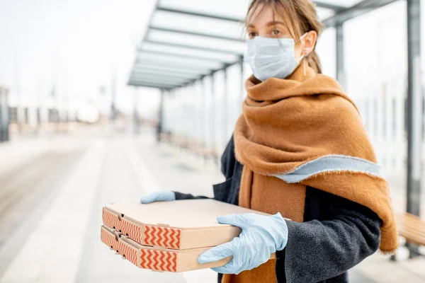 Жінка в медичній масці та рукавичках з вилученням їжі на відкритому повітрі — стокове фото