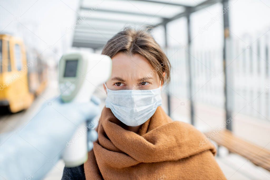 Measuring temperature of a young woman in face mask at a checkpoint outdoors