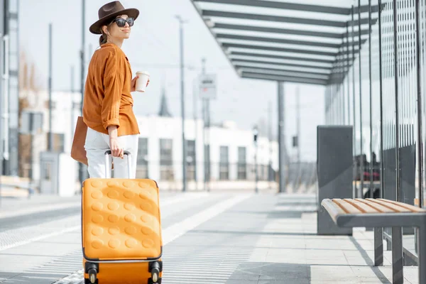Νεαρή γυναίκα ταξιδιώτισσα με μια βαλίτσα στη στάση μεταφοράς — Φωτογραφία Αρχείου