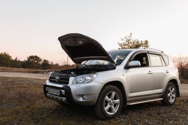 DNIPRO, UKRAINE - FEBRUARY 19, 2020: TOYOTA RAV4 2006 GRAY COLOR WITH OPEN HOOD NEAR THE FOREST, OPEN SPACE IN TWILIGHT