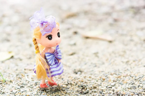 Poppen met het dragen van een paarse jurk Blond haar op het zand. — Stockfoto