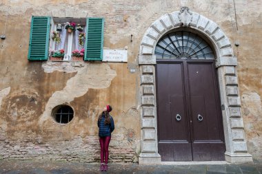 SIENA, İtalya - 13 Mart 2018: Siena, İtalya 'da kocaman kapısı olan eski bir evin önündeki genç kadının geniş açılı resmi