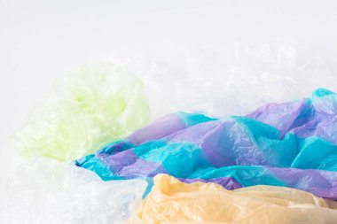 Tek kullanımlık plastik çöp yığını. Beyaz zemin üzerinde yiyecek paketleri ve taşıyıcı çantalar var..