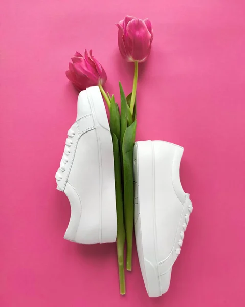 Flat lay of female sneakers with pink tulips on a pink background. Place for your design, text