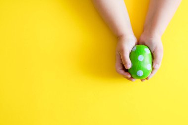 El işi. Paskalya yeşili boyalı ahşap yumurta ve sarı arka planda bir çocuğun ellerinde desen var. en üstteki görünüm