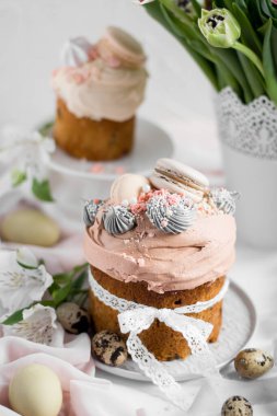 Paskalya pastası kulişi. Beyaz laleli vazonun arka planındaki bir tabakta kremalar ve kurabiyelerle süslenmiş geleneksel paskalya tatlı ekmeği. Boşluğu kopyala