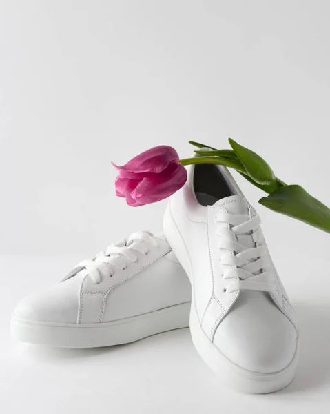흰색 운동화 한 켤레가 분홍색 튤립을 바른 하얀 배경 과 마주 칩니다. 멋지고 운동 선수들을 위한 신발. 봄 산책을 위한 신발 과 유행하는 이미지 — 스톡 사진