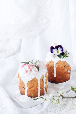 Paskalya Ortodoks tatlı ekmeği, beyaz ahşap bir zeminde beyaz mermer bir tabakta çiçek ve şekerle süslenmiş iki Paskalya pastası..
