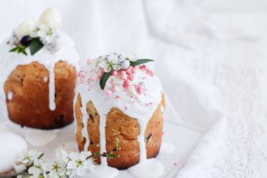 Paskalya Ortodoks tatlı ekmeği, beyaz ahşap bir zeminde beyaz mermer bir tabakta çiçek ve şekerle süslenmiş iki Paskalya pastası..