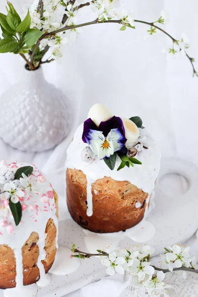 Gâteau de Pâques koulich. Pain de Pâques traditionnel agrémenté d'épis de lièvre et de fleurs lilas Viola tricolor sur une assiette contre un vase blanc aux branches fleuries. Espace de copie — Photo