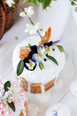 Paskalya pastası kulich. Geleneksel paskalya tatlı ekmeği tavşan kulakları ve leylak çiçekleriyle süslenmiş üç renkli Viola tabakta çiçek açan bir vazoya karşı. Boşluğu kopyala