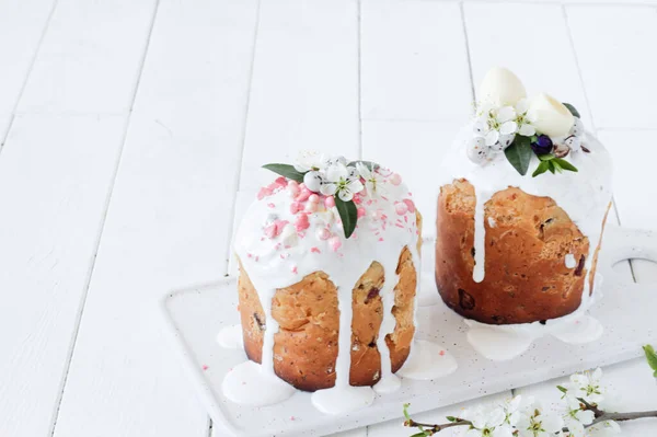 Pain doux orthodoxe de Pâques, deux gâteaux de Pâques décorés de fleurs et de bonbons sur une assiette de marbre blanc sur un fond en bois blanc . — Photo