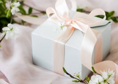 Pembe kurdeleyle sarılmış küçük bir hediye. Çiçekli dalları olan pembe arka planda küçük bir hediye. Küçük bir kutuya odaklanmış sığ alan derinliği.