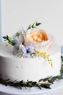 Çiçek ve otlarla süslenmiş beyaz bir pasta bir restorandaki ahşap bir masada duruyor.