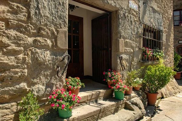 アパートへの別の入り口と明るい鉢植えの花の階段を持つ典型的な古いスペインの家の石積みの壁 ロイヤリティフリーのストック写真