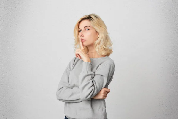 young female wears gray sweatshirt saying hush and pleased to be quiet. siolated over white wall