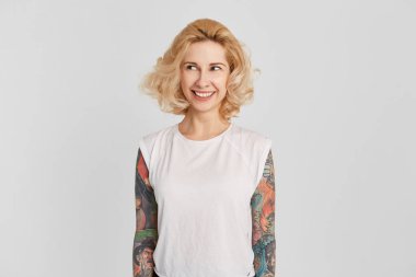 Beyaz casual t-shirt giyen genç sarışın kızın yatay dikey deldi burun mutlu hissediyor ve bir yana görünüyor. pozitif yüz ifadesi. Beyaz bitti izole