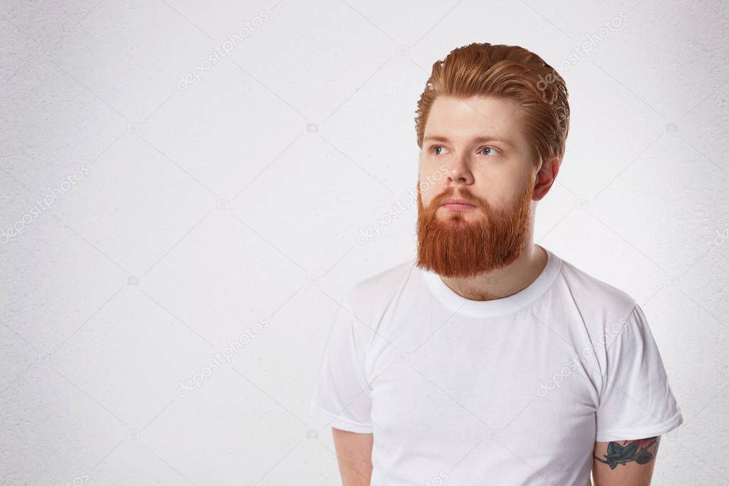 young serious man with ginger beard and hair, looks aside, feels astonished. Isolated with copy space