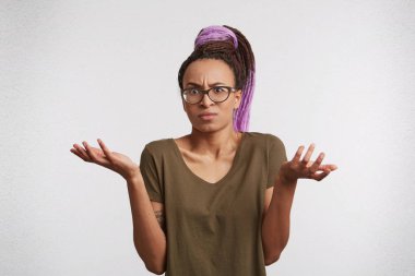 Indoor portrait of doubtful unsure mixed race woman with dreadlocks shrugging her shoulders in auestioning gesture, confused. clipart