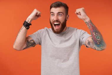 Sakallı, kısa saçlı, neşeli, çekici, esmer adam. En sevdiği takıma tezahürat ederken yumruklarını kaldırıyor. Ağzı açık, turuncu arka planda izole bir şekilde bakıyor.