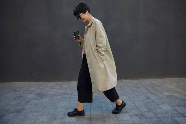 Tarz sahibi, kısa saçlı, iş günü kahve içmeye çıkan, şehir duvarında yürürken şık kıyafetler ve güneş gözlüğü takan, şık, koyu renk saçlı bir kadın.