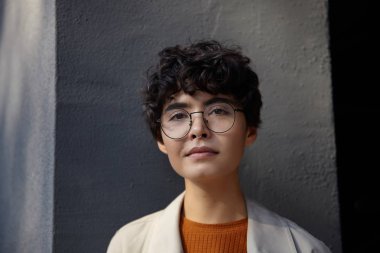 Güzel, kahverengi gözlü, kıvırcık saçlı, kısa saçlı bir kadının portresi. Şehrin çevresinde gözlüklerle dikiliyor, kameraya olumlu bakıyor ve dudaklarını kıvırıyor.