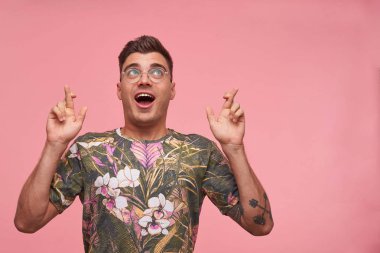 Yakışıklı genç erkeğin daha iyi olmasını umarak pembe arka planda izole edilmiş, yukarı bakan bir stüdyo portresi. Vücut dili kavramı