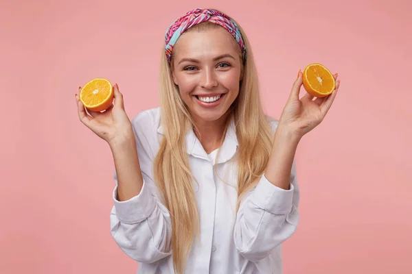 Retrato de linda jovem alegre com metades de laranja em suas mãos, olhando para a câmera com amplo sorriso, isolado sobre fundo rosa — Fotografia de Stock