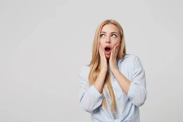 Retrato de mujer rubia encantadora sorprendida con palmas en las mejillas, mirando a un lado con la boca abierta, de pie sobre fondo blanco — Foto de Stock