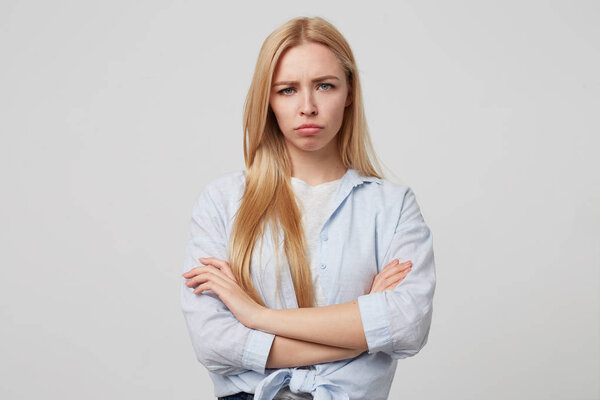 Unhappy attractive blonde female standing over white background with crossed arms, looking sad and going to cry, wearing casual clothes