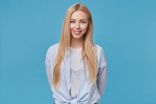 Позитивная привлекательная молодая блондинка в повседневной одежде изолирована на синем фоне, весело смотрит в камеру и демонстрирует свои приятные эмоции. — стоковое фото