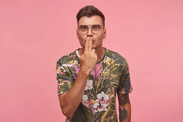 Εσωτερική λήψη του όμορφος νεαρός άνδρας φορώντας γυαλιά και άνθος t-shirt, αναζητούν ενθουσιασμένοι και κάνοντας φιλί αέρα με δύο δάχτυλα, απομονώνονται σε ροζ φόντο — Φωτογραφία Αρχείου