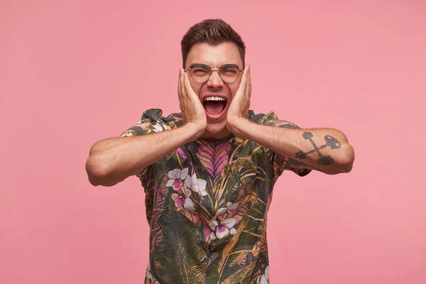 Close-up with young good looking joyful man holding palms on his cheeks, being crazy about happy news, posing over pink background with wide opened mouth — Stock Photo, Image