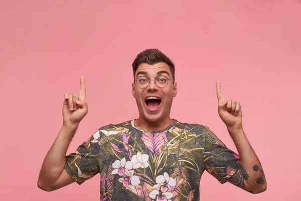 Εσωτερική λήψη του ευτυχισμένη ελκυστική κοντή μαλλιά άνθρωπος σε γυαλιά που αναζητούν κάμερα με υψωμένα χέρια, συστέλλονται μέτωπο και χαμογελά ευρέως στην κάμερα, απομονώνονται σε ροζ φόντο — Φωτογραφία Αρχείου