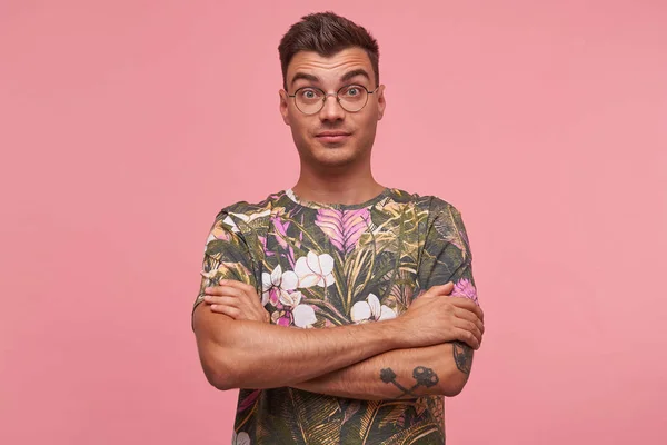 Studio portrait of surprised pretty young man with short haircut standing over pink background, looking puzzled to camera with crossed arms on his chest — Φωτογραφία Αρχείου