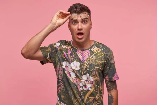Εσωτερική φωτογραφία του έκπληκτος υπέροχο νεαρό κοντό μαλλί άνδρα σε άνθος t-shirt στέκεται πάνω από ροζ φόντο, κινείται γυαλιά στο μέτωπο με κατάπληκτος βλέμμα — Φωτογραφία Αρχείου