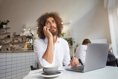 Genç çekici, uzun saçlı iş adamı ofis dışında bilgisayarla konuşurken Luncheonette 'te kahve içerken telefonla konuşuyor.
