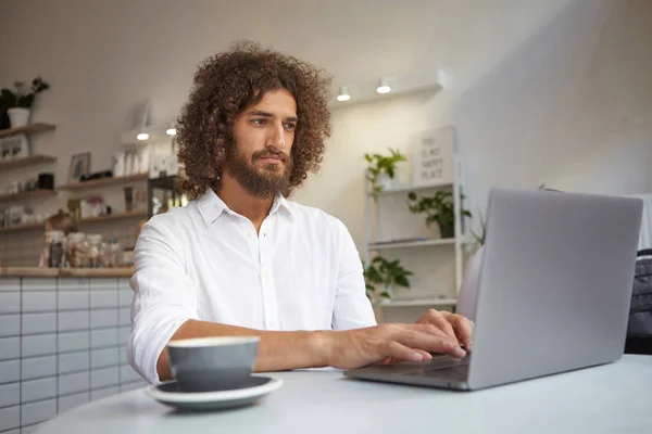 Svår hane bär vit skjorta kontrollera e-post på nätet, med hjälp av modern bärbar dator, arbetar på distans på projekt, hålla händerna på tangentbordet, med en kopp kaffe — Stockfoto