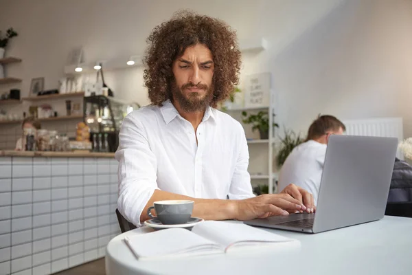 수염을 기른 젊은 매력적 인 사업가 가현 대식 노트북을 가지고 카페에서 원격으로 일하면서 키보드에 손을 얹고 자신의 노트를 열심 히들여다보고 있다 — 스톡 사진