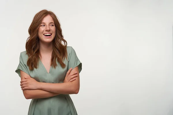 Jovem mulher bonita feliz com cabelo vermelho posando sobre fundo branco com braços cruzados, olhando para o lado com sorriso largo e sincero, vestindo vestido vintage na cor pastel — Fotografia de Stock