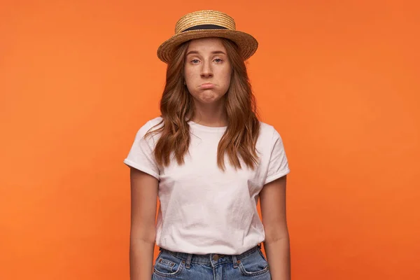 Студийное фото милой рыжеволосой девушки, позирующей на оранжевом фоне с расстроенным лицом, смотрящей в камеру и гримасничающей, позирующей на оранжевом фоне — стоковое фото