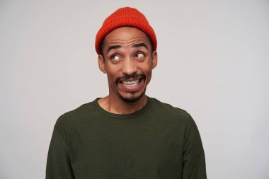 Neşeli, genç, koyu tenli, esmer, sakallı, beyaz, mükemmel dişlerini gösteren, kameraya yüzünü buruşturan, beyaz arka planda poz veren adam.