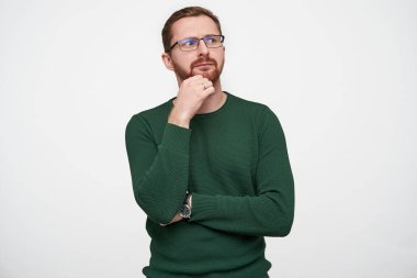 Bilmece gibi, genç, güzel, kısa saçlı, kısa saçlı, eli çenesinin altında, kaşları çatık, beyaz arka planda dikilen bir erkek.