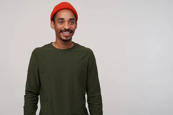 Encantador jovem de olhos castanhos barbudo morena macho com pele escura olhando positivamente de lado e sorrindo amplamente, estar em bom humor enquanto posando sobre fundo branco — Fotografia de Stock