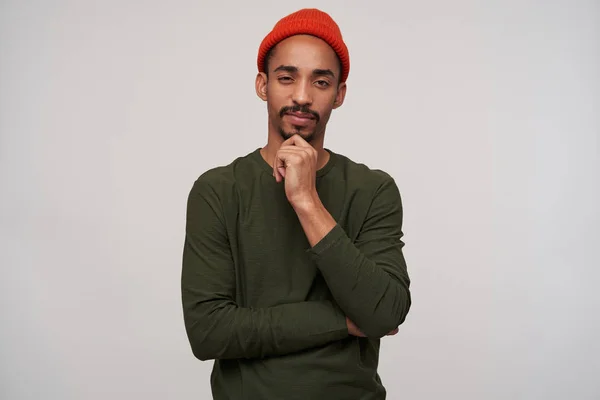 Thoughtful young bearded dark skinned brunette guy holding his chin and squinting while looking at camera, wearing casual clothes while posing over white background — 스톡 사진