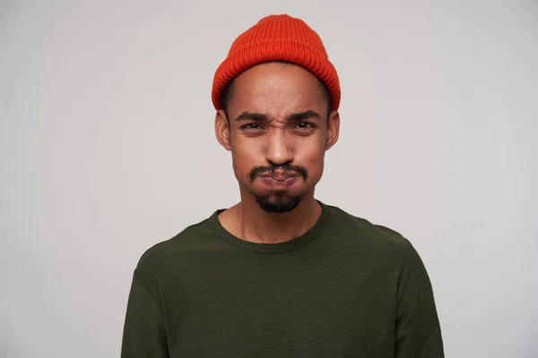 Portrait of young brown-eyed bearded dark skinned male taking air into his mouth and puffing out cheeks while looking to camera, standing against white background — 스톡 사진
