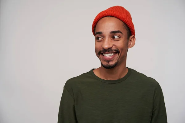 Vrolijke jonge mooie donkere huid brunette hipster met baard kijken positief opzij met charmante glimlach, verheugen over het ontmoeten van vrienden, geïsoleerd over witte achtergrond — Stockfoto