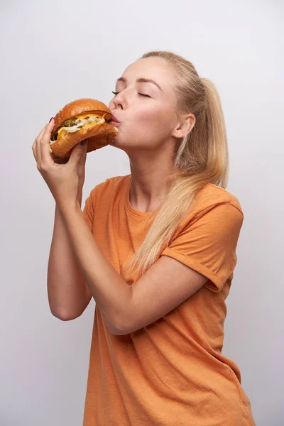 Indoor photo of pleasant looking young blonde female in casual clothes keeping her eyes closed while foretasting delicious meal, standing against white background — kuvapankkivalokuva