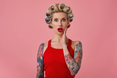 Açık gözlü, sarışın, dövmeli ve makyajlı güzel bir kadın. Yanağında avuç içi makyajıyla kameraya bakıyor. Yaklaşan partiye hazırlanıyor.